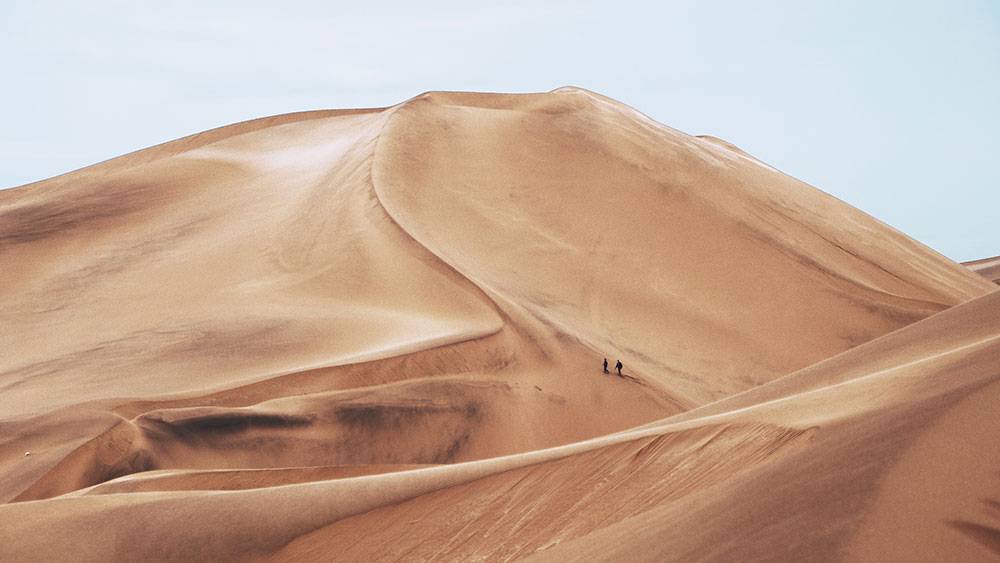 Two people in the distance walking across sand dunes in a desert.