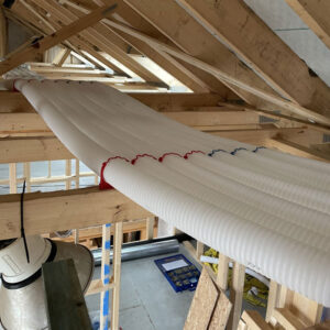 White plastic pipes running across wooden beams in the attic of a house under construction.