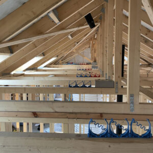 A close up of an attic full of exposed wooden beams and a blue and red ventilation system with metal ducts sitting on the beams.