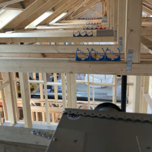 A close up of an attic full of exposed wooden beams and a blue and red ventilation system with metal ducts sitting on the beams.