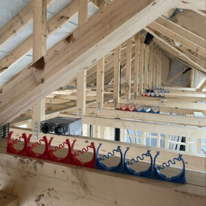 An attic full of exposed wooden beams and a blue and red ventilation system with metal ducts sitting on the beams.