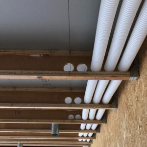 White plastic pipes running through holes in a wooden beams in a building.