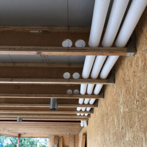 White plastic pipes running through holes in a wooden beams in a building.