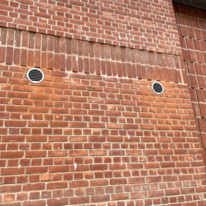 A red brick wall with two round air filters in the middle of the wall spread apart.