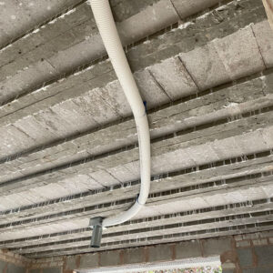 A white plastic pipe running across a concrete ceiling and being fed into a metal duct.