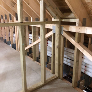 A collection of white plastic pipes running through wooden beams inside an attic.