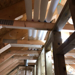 A collection of white plastic pipes running through wooden beams inside an attic.