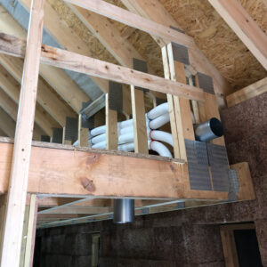 A collection of white plastic pipes running through wooden beams in an attic of a building.