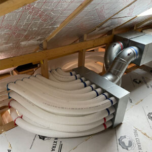 A ventilation system with a bunch of white plastic pipes being fed into the metal duct in an attic.