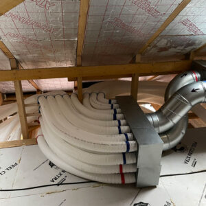 A ventilation system with a bunch of white plastic pipes being fed into the metal duct in an attic.