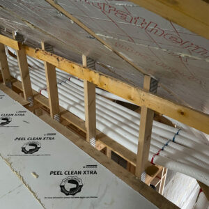 White plastic pipes running along the attic surrounding by wooden beams.