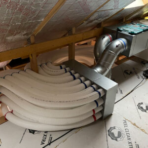A ventilation system with a bunch of white plastic pipes being fed into the metal duct in an attic.