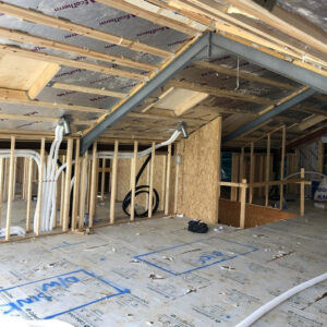 An attic under construction with exposed wooden beams and white plastic pipes running across it.