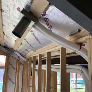A close up of a ceiling in a building under construction with exposed wooden beams and white plastic pipes running across it.