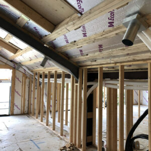 A close up of a ceiling in a building under construction with exposed wooden beams and white plastic pipes running across it.