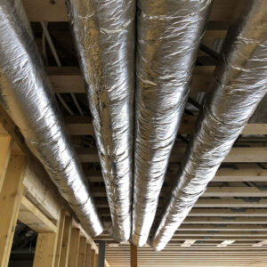 Four metal pipes running crossing the ceiling of a building under construction with exposed wooden beams.