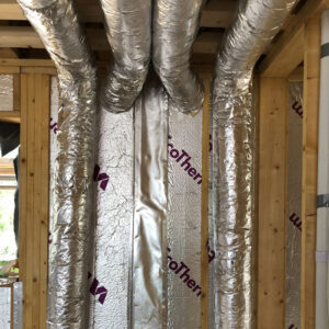 A close up of four metal pipes running crossing the ceiling of a building under construction with exposed wooden beams.