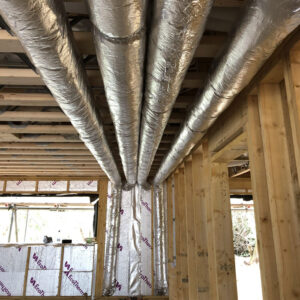 Four metal pipes running crossing the ceiling of a building under construction with exposed wooden beams.