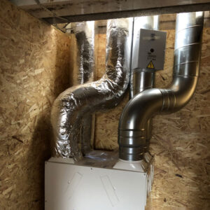 A close up of a ventilation system inside chipboard consisting of metal pipes with a warning sign on them.