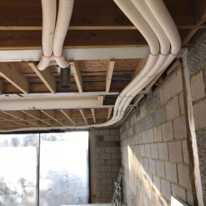 A close-up photo of a ceiling with exposed white insulated pipes running across it in a building under construction.