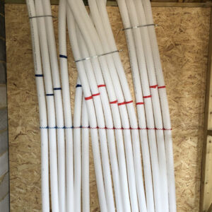 A row of white PVC pipes with threaded ends lie on a wooden table.