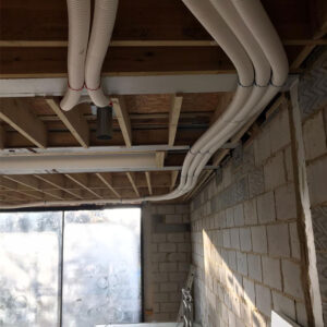 A close-up photo of a ceiling with exposed white insulated pipes running across it in a building under construction.