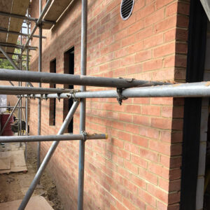 A close up of a building under constructin with red bricks being supported by metal scaffolding.