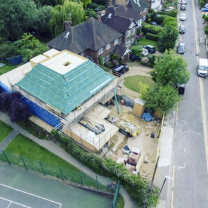 An aerial view of a building under construction with a pyramidal roof being hoisted into place.