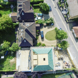 An aerial view of a building under construction with a pyramidal roof being hoisted into place by a crane.