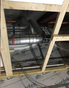 Close-up of a section of an unfinished attic under construction. Exposed metal pipes with insulation. Branding on the pipes includes "Caberdek", "Norbord", "BBA". There is also a metal bracket attached to the pipes.