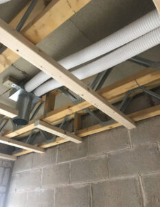 White plastic pipes running through a hole in a ceiling surrounded by wooden beams and exposed brick.