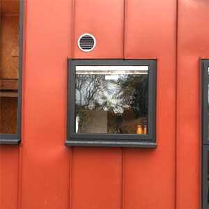A window with a white frame and multiple small panes sits on the side of a red building.